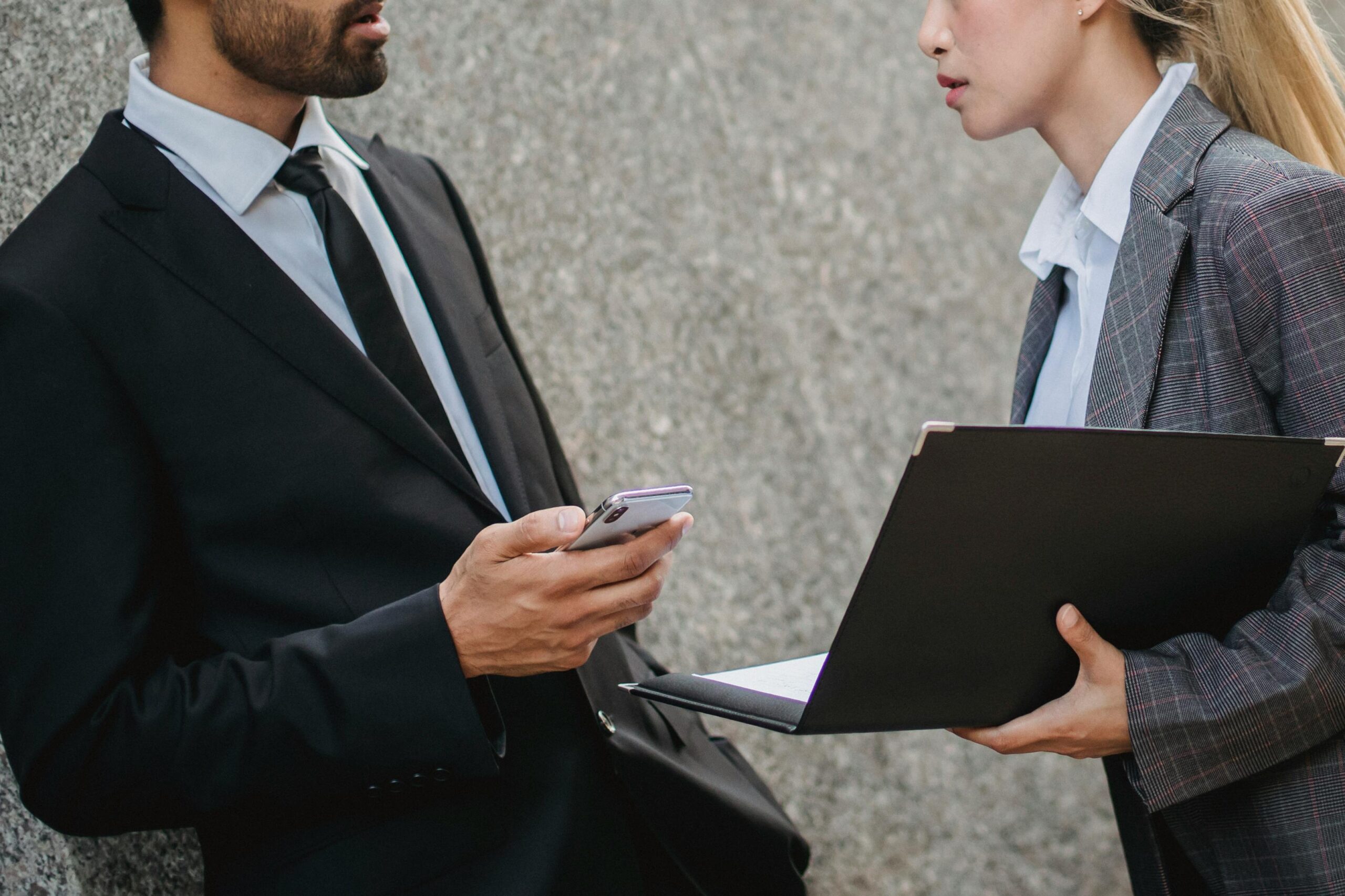 Business professionals in formal wear discussing while holding a laptop and phone.